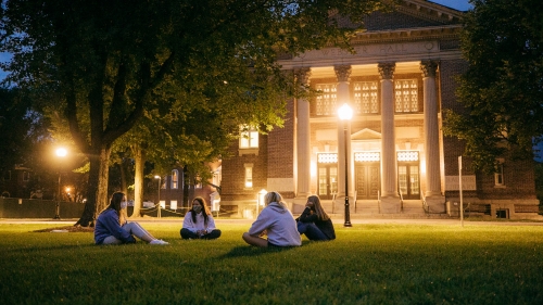 Students sit on the green at night